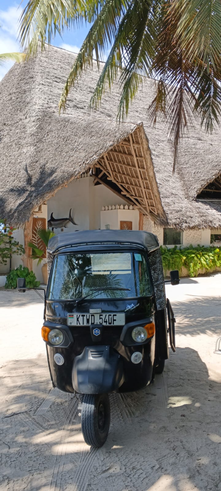 Tuk tuk parked in front of a Swahili thatched-roof villa in Watamu