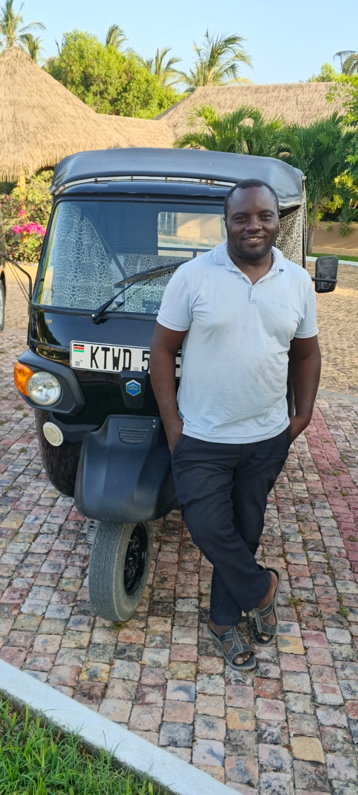 Mose standing next to his black tuk tuk in Watamu, Kenya